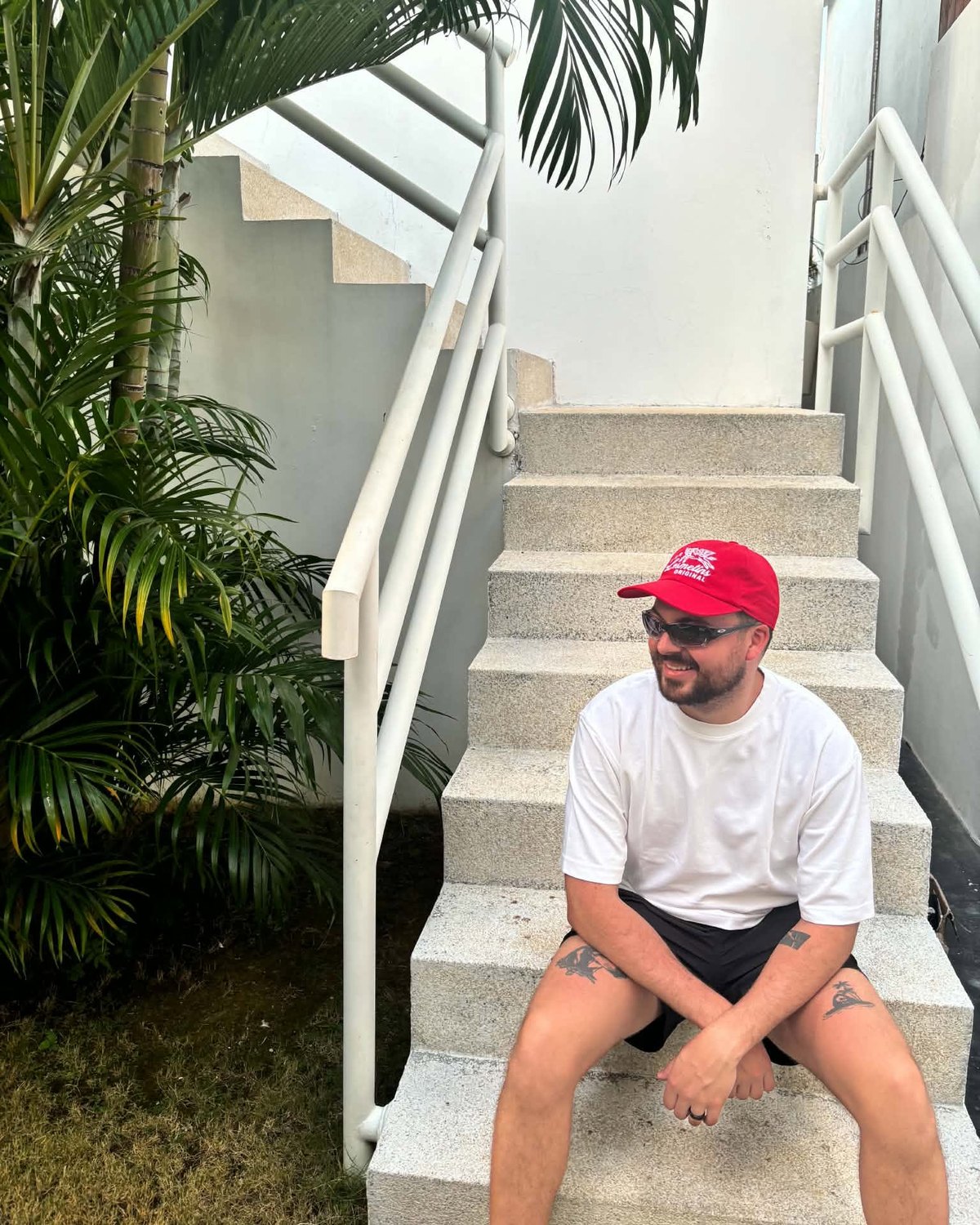 Calvin, the designer behind CALURTS, sitting on white stairs in a red cap